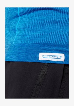 Maglietta sportiva blu con un design a maglia testurizzata. Orlo rifinito con un'etichetta bianca che reca la scritta "CLIMATYL". Abbinata a pantaloni corti neri.