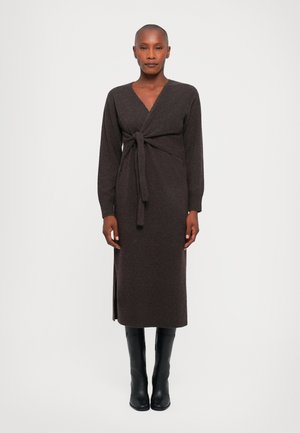 Braunes Strick-Wickelkleid mit langen Ärmeln, Taillierungsdetail und Seitenschlitz. Kombiniert mit schwarzen, knielangen Stiefeln mit strukturierter Oberfläche.