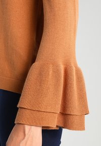 Trui in roestkleur met gelaagde, uitlopende geribbelde manchetten. Zachte textuur, getailleerd, eenvoudig ontwerp en een klassieke ronde halslijn.