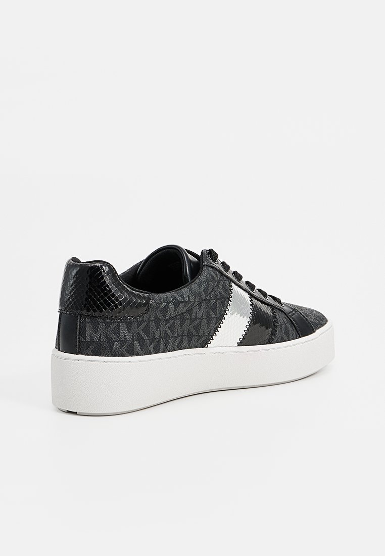 Zapatillas negras con una parte superior texturizada y patrones sutiles, una franja blanca en contraste y una suela blanca gruesa. Detalles suaves y brillantes.