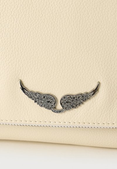 Peňaženka krémovej farby s textúrovaným povrchom. Má strieborný akcent v tvare krídla s dekoratívnymi detailmi a kontrastným prešitým okrajom.