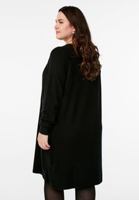 Svart långärmad cardigan med avslappnad passform, mjuk textur och sidoklyftor, med rundad halsringning och ribbade manschetter.