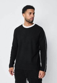 Sweatshirt noir avec une bordure accentuée blanche autour du cou et le long des manches ; fabriqué dans un matériau doux, présentant une coupe simple et décontractée.