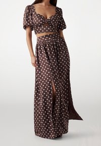 Brązowy top w kropki z krótkimi rękawami i detalem w postaci kokardy, w połączeniu z długą, zwiewną spódnicą maxi z wysokim stanem i bocznym rozcięciem.