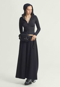 Black athletic zip-up hoodie with a hood, paired with a long black skirt and a black fanny pack; grey sneakers complete the outfit.