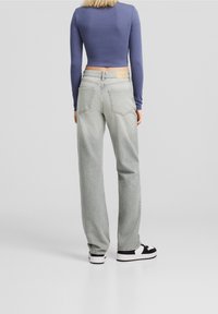 Jeans de tiro alto en gris claro, con un corte relajado. Presentan bolsillos traseros, una etiqueta de cuero rectangular en la cintura y un diseño de pierna recta.