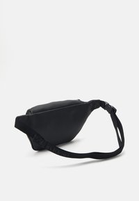 Mustan, teksturoitu synteettinen olkalaukku, jossa on kaareva muoto, säädettävä hihna ja vetoketjusuljenta. Mukana on logo kaiverrettuna hihnaan.