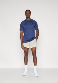 Ναυτικό μπλε αθλητικό μπλουζάκι Nike με υφή, σε συνδυασμό με ανοιχτό μπεζ σορτς. Το μοντέλο φοράει λευκά αθλητικά παπούτσια και κάλτσες που ταιριάζουν.