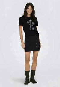 Sort t-shirt med hvid dandelion grafik og tekst, parret med en sort knap-foran nederdel; båret med sorte knæhøje støvler.