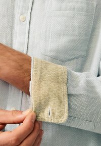 Svijetloplava teksturirana košulja sa bež uzorkastim manžetama, koja se zatvara na dugmiće i ima jednu džep na prsima.