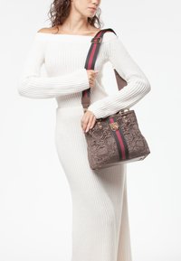 Bolso marrón texturizado con diseño floral en relieve, que presenta una correa rayada multicolor y acentos de hardware dorado.