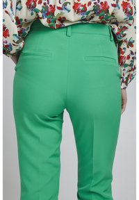 Gröna skräddarsydda byxor med en slät textur, smal passform och bakfickor. Midjan har bälteshällor för extra detalj.