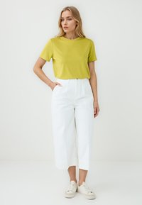 T-shirt verde lime a manica corta abbinato a pantaloni bianchi a vita alta e larghi, con sneakers di colore chiaro. Design semplice e vestibilità rilassata.