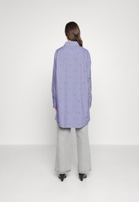Langærmet, knap-op skjorte i lavendel med små, mørke mønstre. Har en buet kant og en afslappet pasform, parret med vidde bukser i lys grå.
