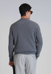 Grauer gerippter Pullover mit rundem Ausschnitt, der über ein strukturiertes Design und einen enganliegenden Bund verfügt, kombiniert mit hellgrauen Hosen.