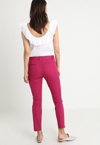 Pantalon ajusté fuchsia avec poches et taille mi-haute. Associé à un haut blanc avec un col à volants et un tissu texturé.