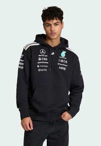 Sweat à capuche noir avec poche avant, capuche à cordon de serrage et logos en blanc et turquoise. Caractéristiques des rayures grises sur les épaules. Matière en mélange de coton.