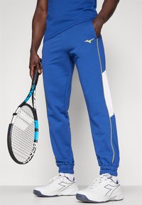 Blue athletic pants with yellow side stripes and a white panel, made of soft fabric, featuring cuffed ankles and a slim fit design.