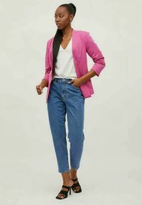 Un sacou roz, croit pe corp, peste un top alb, asortat cu blugi deschiși la culoare, cu talie înaltă. Sandale negre cu toc pun în evidență ținuta.