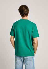 Green cotton t-shirt with short sleeves, crew neck, and relaxed fit, worn with light blue denim jeans. Smooth texture, minimal design.
