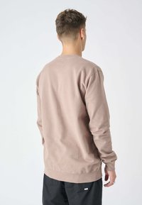 Brown long-sleeve sweatshirt featuring a crew neck, soft texture, and ribbed cuffs. Back view shows a relaxed fit and minimal branding detail.