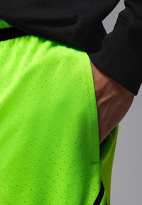Shorts de sport vert fluo à haute visibilité, avec une texture perforée, dotés d'une ceinture noire et de détails de poche sur le côté.