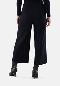 Marineblaue, weit geschnittene Hose mit hoher Taille und plissiertem Design, kombiniert mit schwarzen Stöckelschuhen. Glatte Textur und taillierte Passform.