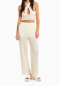Szydełkowy top typu crop z wycięciem na dekolcie, zestawiony z szerokimi spodniami z wysokim stanem. Oba w jasnokremowym kolorze z teksturowanym wzorem.