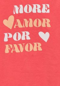T-shirt corail avec un texte multicolore indiquant "MORE AMOR POR FAVOR". La police est ludique avec des formes et des tailles variées.