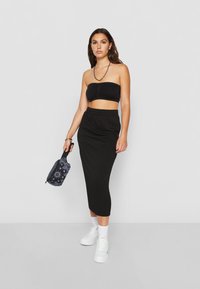 Haut bandeau noir et jupe midi noire côtelée, associés à des baskets blanches. Portant un sac à motifs noir et blanc. Texture lisse.