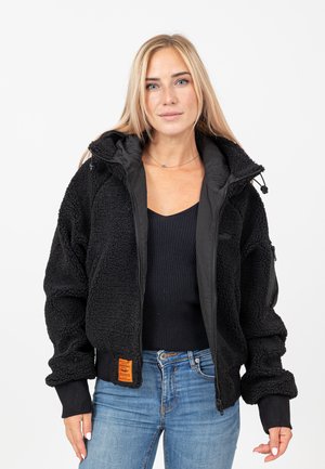 Zwarte fleece bomberjack met een gestructureerde buitenkant, ribgebreide boorden en ritszakken. Voorzien van een oranje label aan de onderkant.