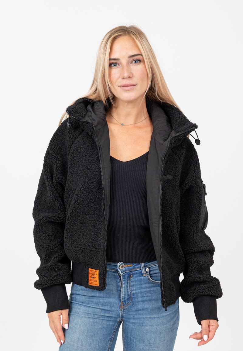 Veste bomber en polaire noire avec un extérieur texturé, des poignets côtelés et des poches zippées. Comprend une étiquette orange sur le côté inférieur.