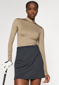 Garmai piedurknēm, brūns tops ar augstu apkakli. To papildina melna, strukturēta, plisēta svārku. Iespējas priekšējām kabatām un golfa nūja rokā.