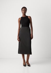 Top in maglia nera con un design testurizzato, abbinato a una gonna midi nera liscia. Outfit completato con décolleté neri a punta. Linee pulite, dettagli minimi.