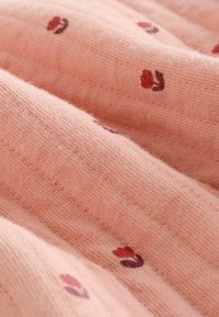 Blød rosa stof med en tekstureret vævning, der har små blomstermønstre i rustrøde og mørkelilla farver, hvilket skaber et delikat design.
