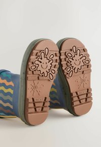 Gummiregenstiefel mit blauem Obermaterial, das wellenförmige, mehrfarbige Muster aufweist, und einer braunen strukturierten Sohle mit Spritzdesign und Smiley-Gesicht.