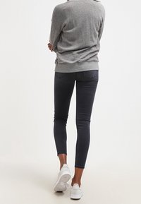 Suéter gris combinado con jeans oscuros y zapatillas blancas. El suéter tiene un corte relajado y los jeans son ajustados con bolsillos traseros.