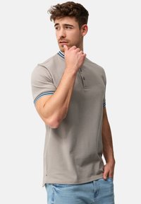 Polo shirt grigio chiaro con una placca a tre bottoni, colletto a coste con strisce blu e bianche, e maniche corte.