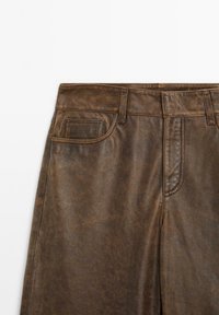 Brown faux leather pants featuring a waistband, side and back pockets, and stitched detailing for added texture.