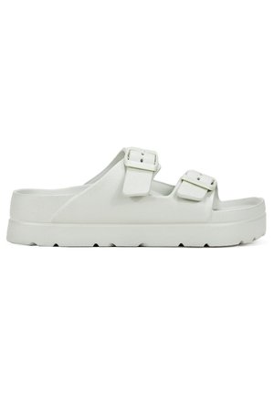 White sandals feature two adjustable buckles, a textured upper, and a thick, ridged sole for traction. Simple design and open-toe style.