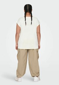 T-shirt bianca a maniche corte con una vestibilità rilassata, abbinata a pantaloni cargo beige larghi con tasche laterali e sneakers bianche.