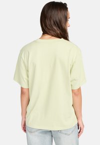 Light green oversized cotton t-shirt with short sleeves and a round neckline, displayed from the back. Hemline falls below the waist.