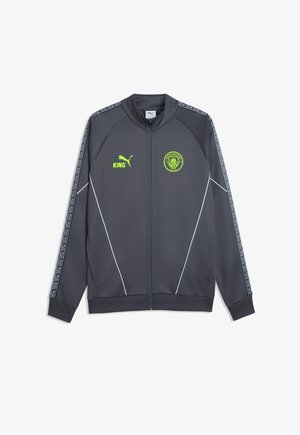 Dunkelgraue Sportjacke mit durchgehendem Reißverschluss, neon-gelbem Manchester City Wappen und Puma-Logo, gemusterten Streifen an den Ärmeln und weißen Paspeldetails.