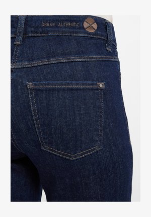 Donkerblauwe denim jeans met een gestructureerd oppervlak, voorzien van een rechthoekige achterzak, minimalistische stiksels en een label met de opdruk "DREAM AUTHENTIC."