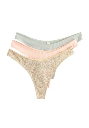 Donna con capelli lunghi intrecciati in piedi a piedi nudi che indossa un reggiseno azzurro chiaro con bordatura di pizzo e biancheria intima coordinata su sfondo bianco uniforme.