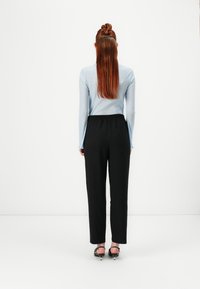 Lyseblå, ribbet langærmet top parret med sorte, højtaljede bukser. Modellen har lige rødt hår stylet i en topknude.