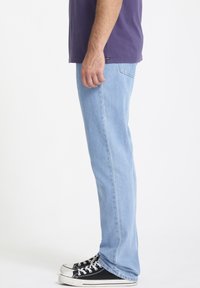 Jean en denim bleu clair avec une coupe droite, portés avec des baskets noires et blanches, affichant une coupe décontractée et des coutures visibles.