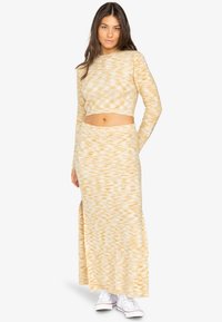 Ensemble en tricot bicolore jaune et blanc, composé d'un haut court et d'une jupe haute fendue, associé à des baskets blanches. Texture douce, design ajusté.