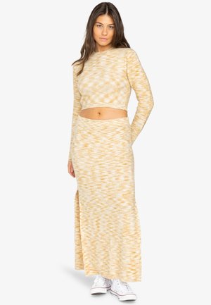 Ensemble en tricot bicolore jaune et blanc, composé d'un haut court et d'une jupe haute fendue, associé à des baskets blanches. Texture douce, design ajusté.