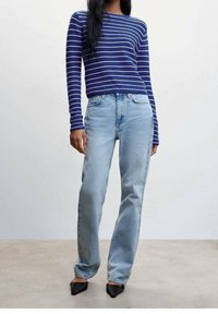 Femme portant un haut à manches longues bleu et blanc à rayures, un jean taille haute bleu clair à jambes droites et des chaussures noires pointues.